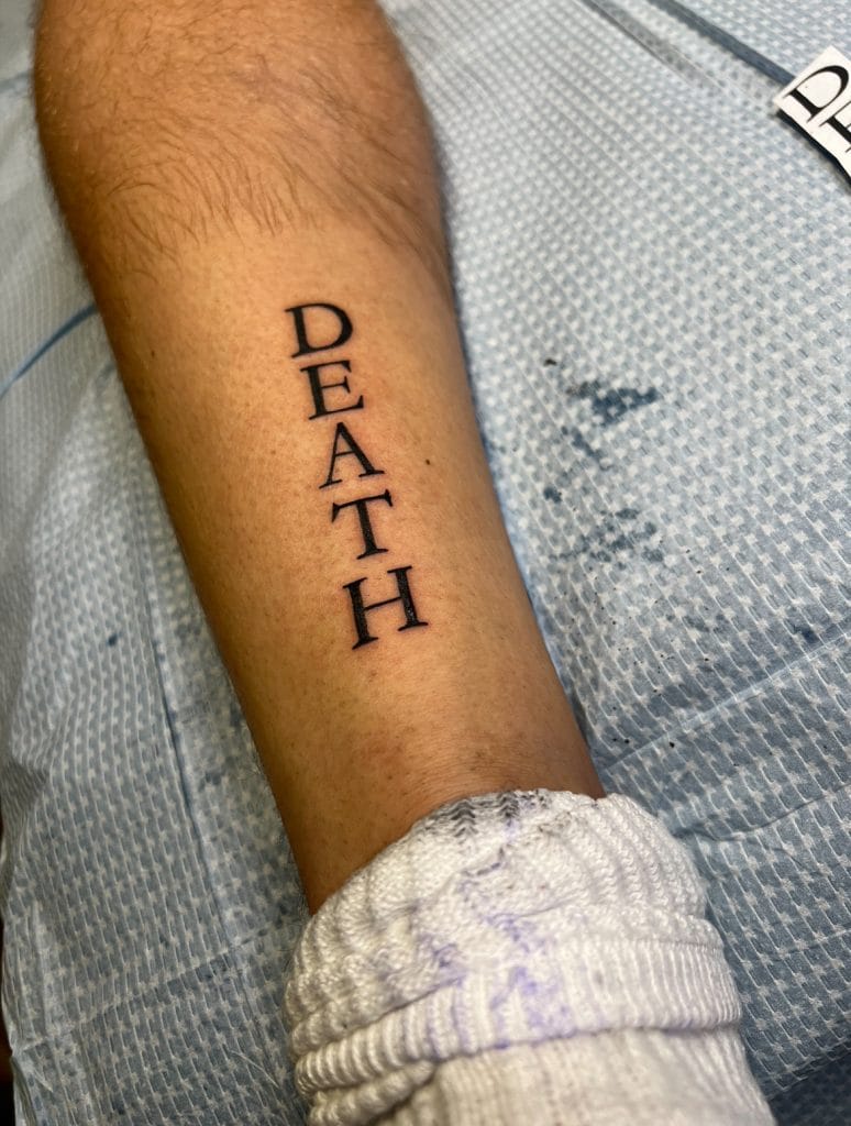 Tattoo of the word DEATH vertically on a persons forearm.
