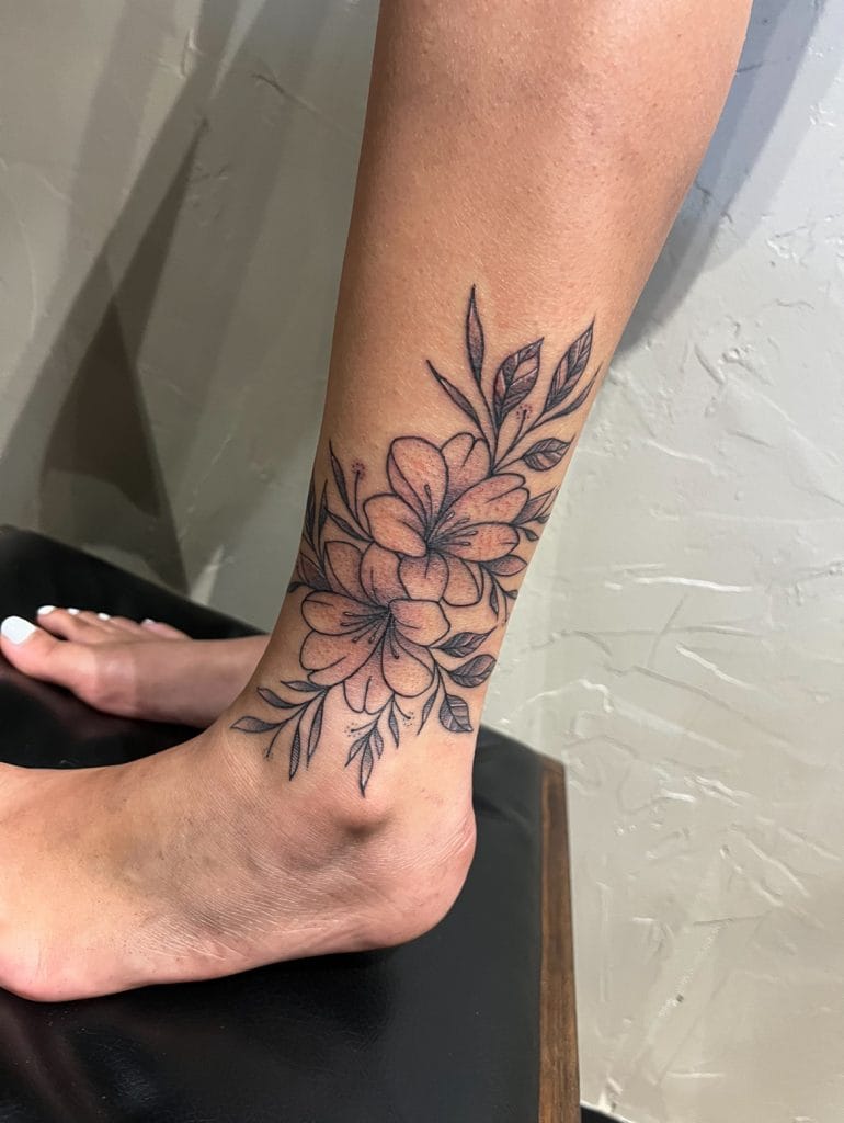 Pink and black floral tattoo on ankle and lower leg with leaves and petals.