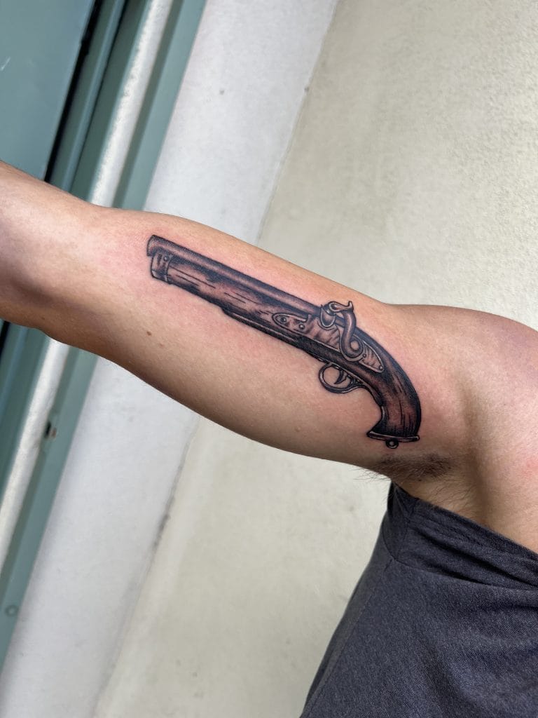 Tattoo of a vintage flintlock pistol on upper arm.