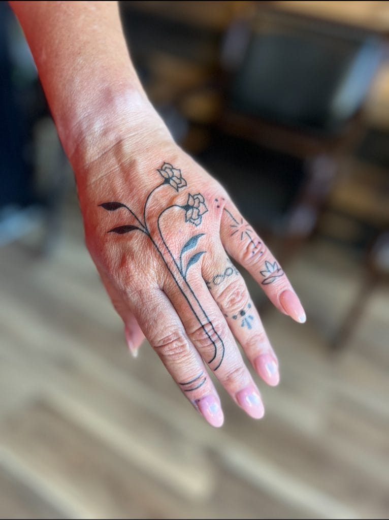 Hand with a floral tattoo featuring a small flower, leaves, and abstract designs.