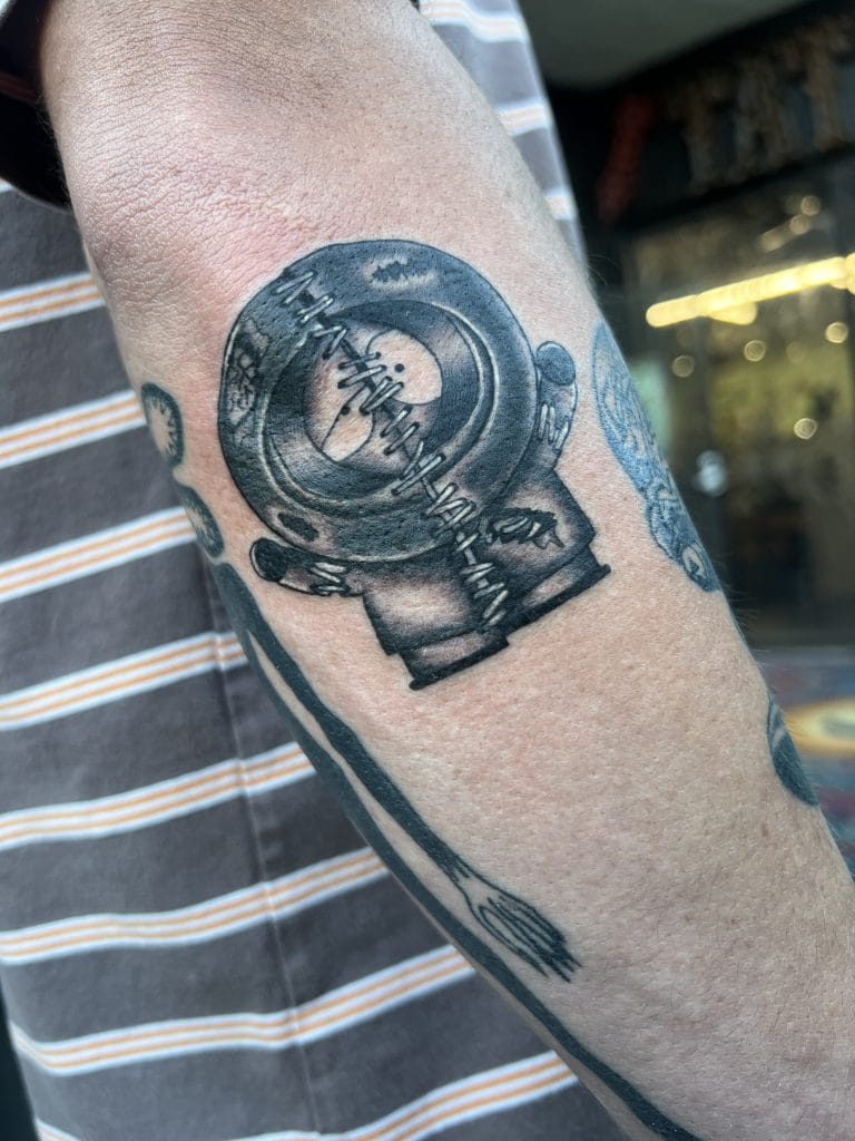 Tattoo of a vintage coffee grinder with a spoon extending downward, on persons arm.