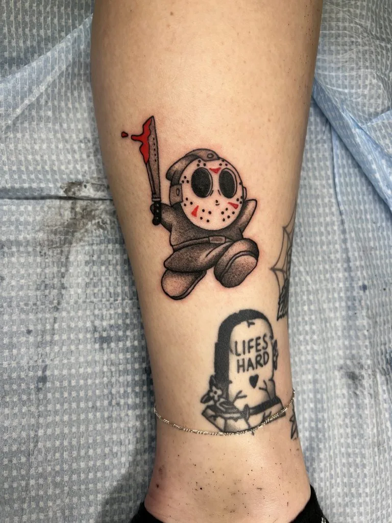 Tattoo of a cartoon character dressed as a horror movie killer holding a blood-dripping axe.