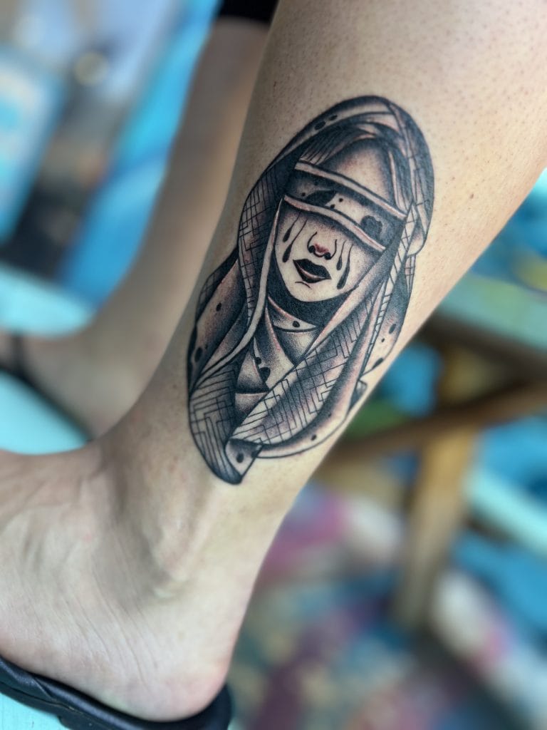 Black and gray tattoo of a woman with long hair, wearing a blindfold and tears on her face.