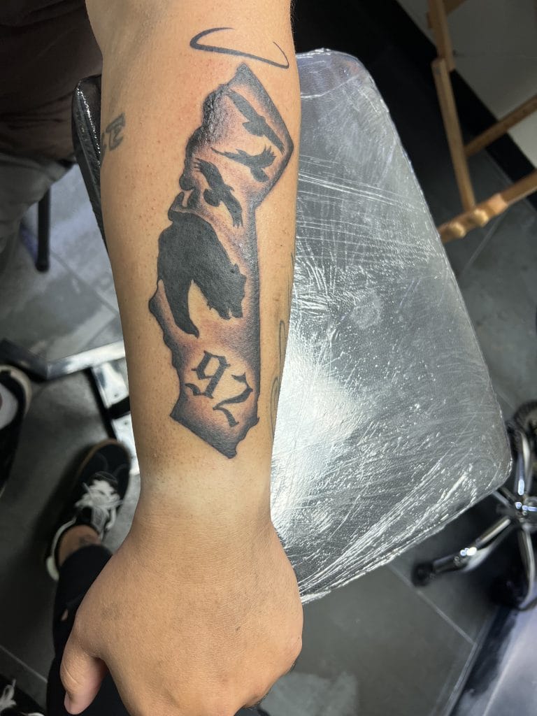 Tattoo of a wolfs head, a halo, and the number 972 on the forearm.
