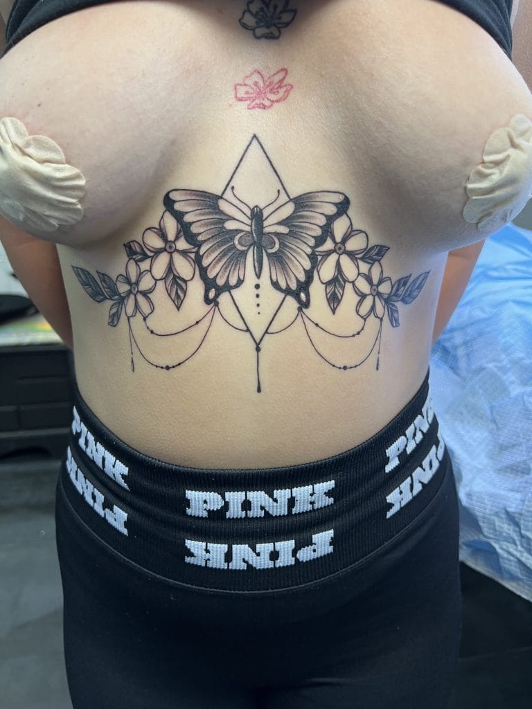 Black butterfly and floral tattoo with geometric lines on persons chest and upper abdomen.
