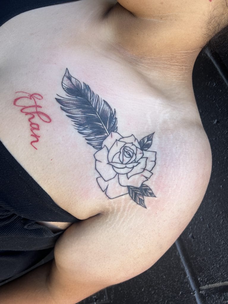 Black and white rose with a feather and red cursive hope tattoo on shoulder.