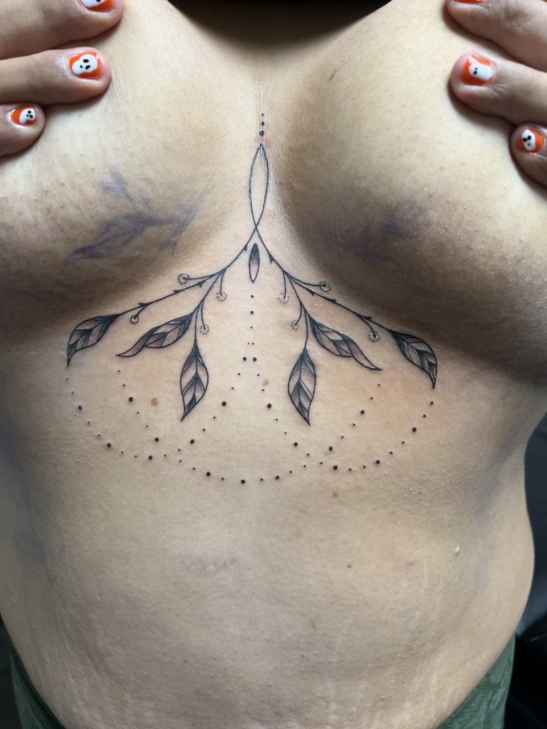 Black floral and dotted tattoo design on the lower chest above the stomach.
