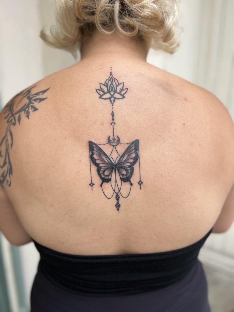 Black butterfly tattoo with geometric and celestial elements on upper back.