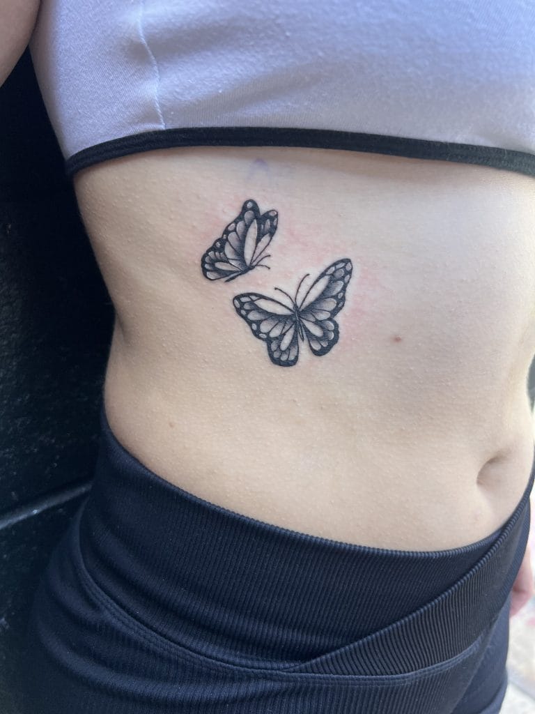 Two black and white butterfly tattoos on persons side waist, above waistband.