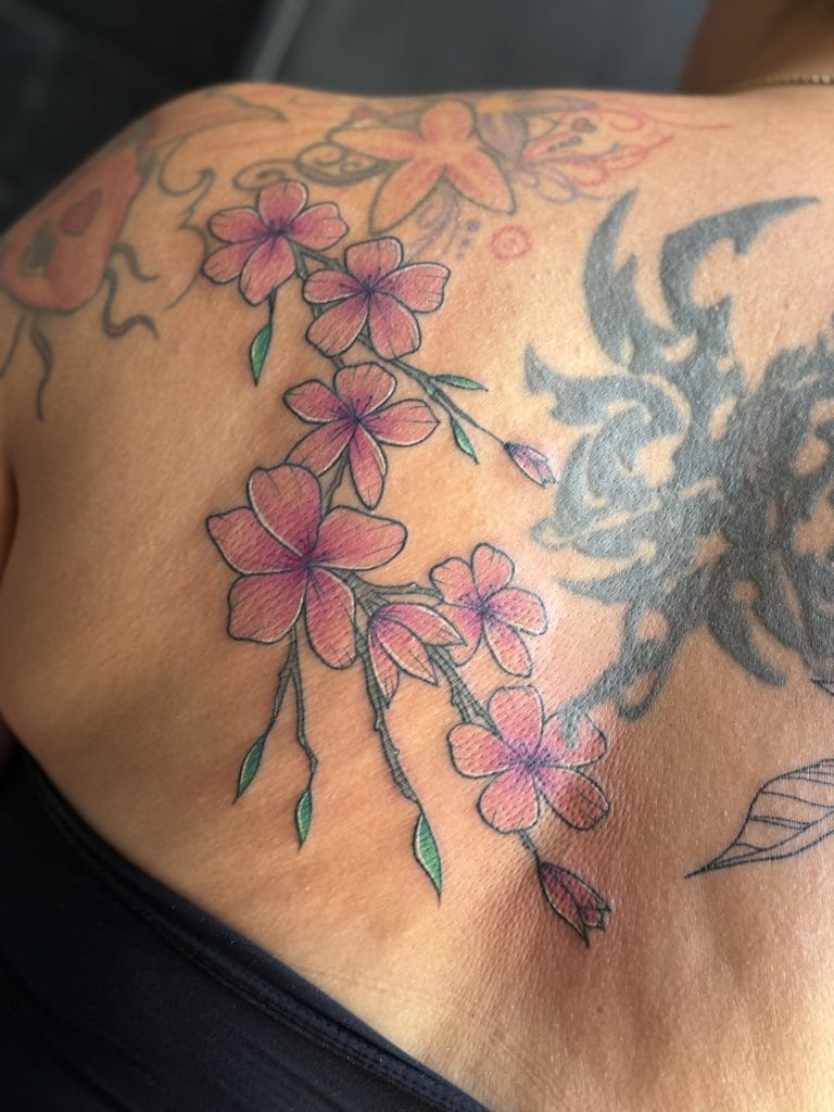 Pink cherry blossom flowers with green leaves on a persons shoulder and chest.