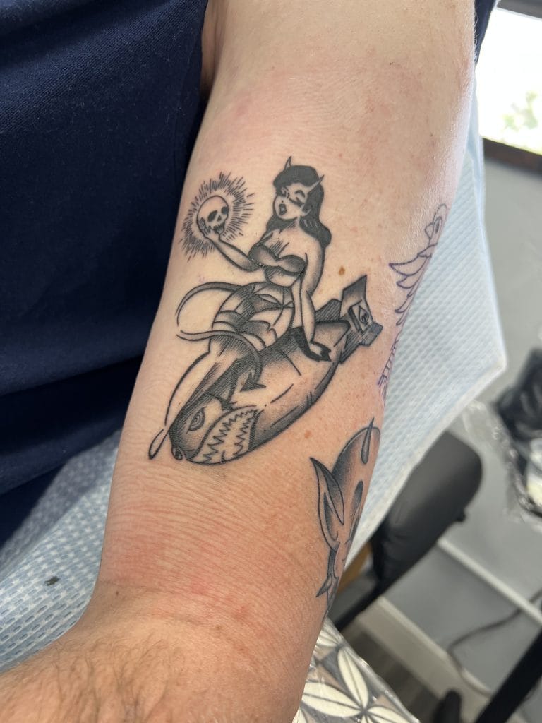 A woman with devil horns holding a skull, sitting on a shark with an open mouth.