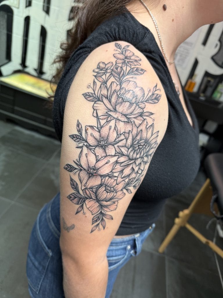 Black and gray floral tattoo on upper arm with large blooming flowers and leaves.