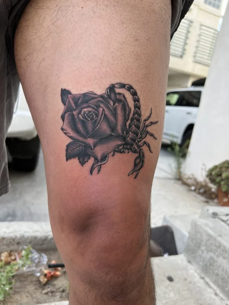 Black and gray tattoo of a rose with a scorpion on a persons thigh.