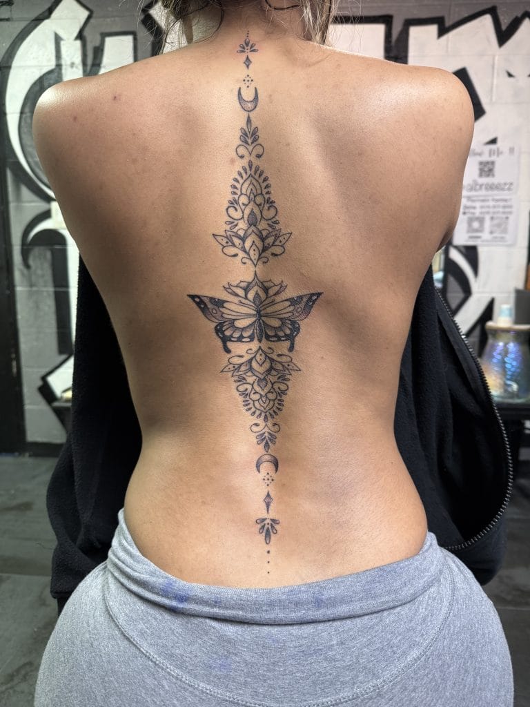Vertical symmetrical tattoo with floral, butterfly, and celestial moon designs down the spine.