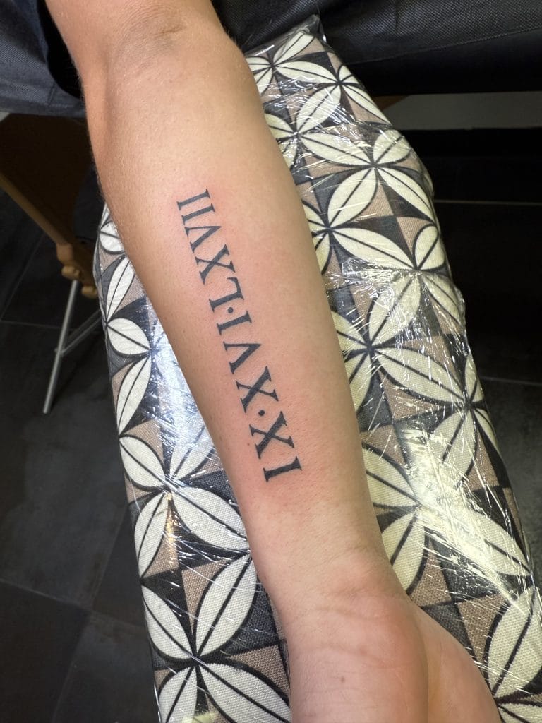 Roman numerals I.X.II.XL.XI tattooed vertically on forearm.