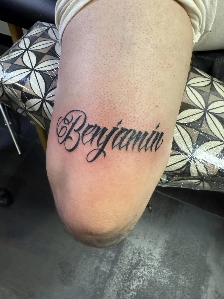 Bold black tattoo of the word Beyoncé in cursive script on a persons thigh.