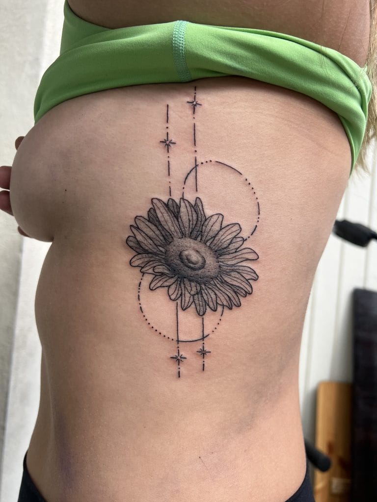 Black and gray sunflower tattoo with geometric lines and star accents on persons side.