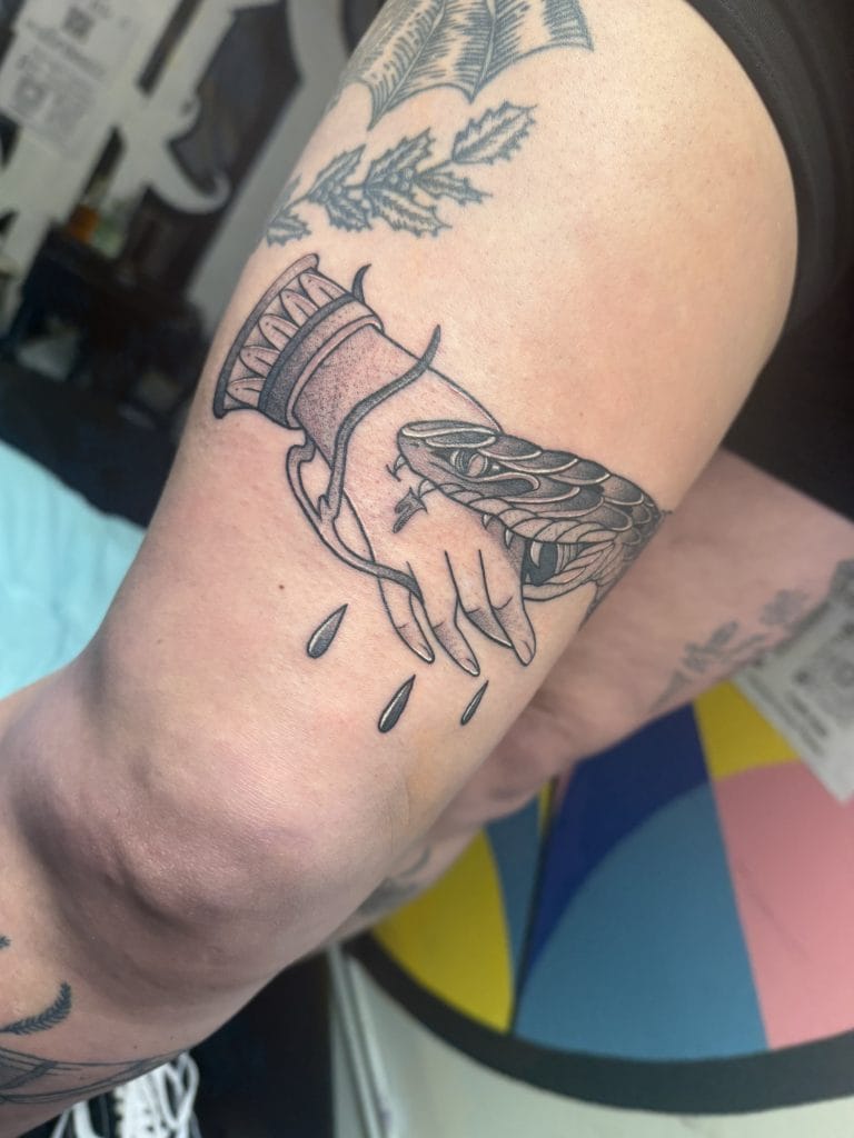 Black and gray tattoo of a hand with a snake wrapped around it, dripping ink.