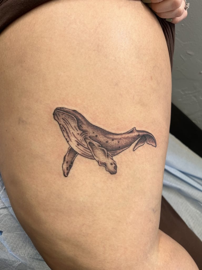 Black and gray whale tattoo on upper thigh, detailed with shading and spots.