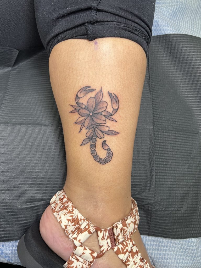 Tattoo of a scorpion with floral elements on the lower leg.
