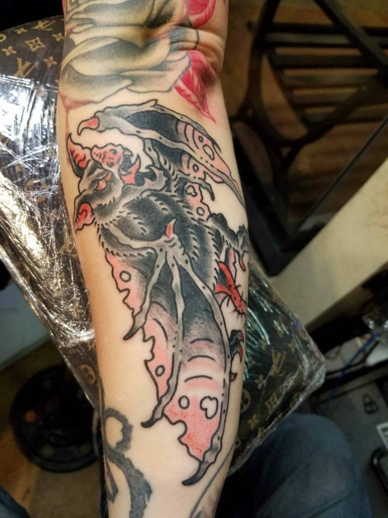 Black and red tattoo of a moth with detailed wings on a persons forearm.