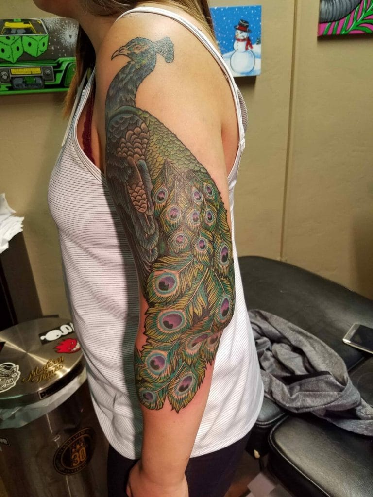 Colorful peacock tattoo covering the upper arm and shoulder of a person.