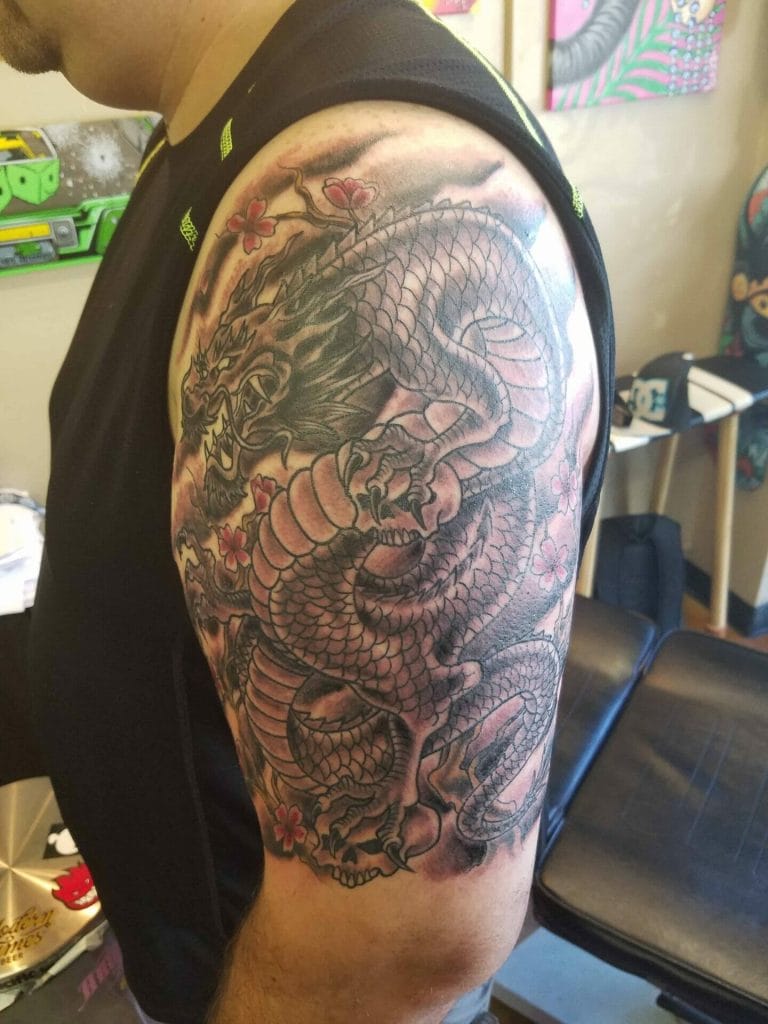 Black and gray dragon tattoo with pink cherry blossoms on persons upper arm.