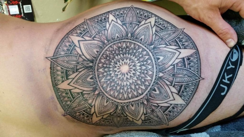 Detailed black and gray mandala tattoo on upper thigh with intricate geometric patterns.