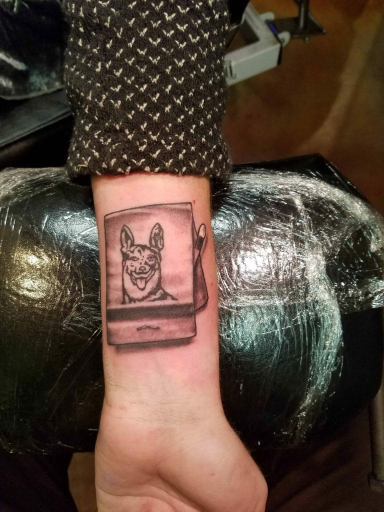 Tattoo of a dog’s face on a tablet screen on a persons forearm.