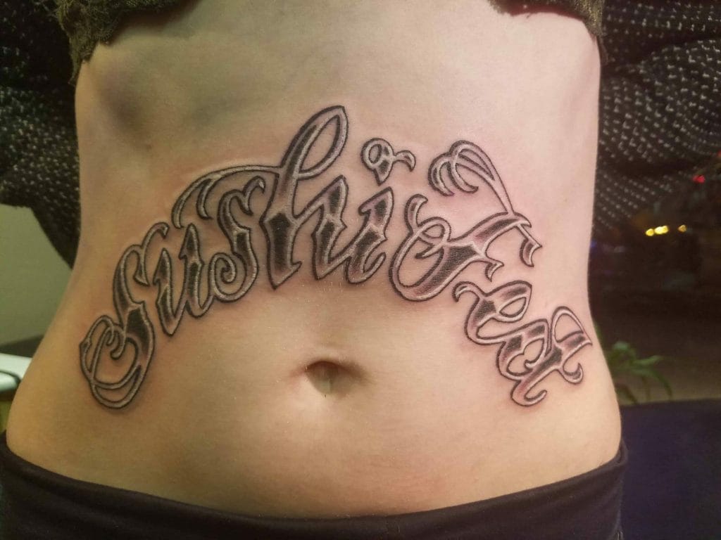 Tattoo reading Trust in ornate cursive script across the lower abdomen.