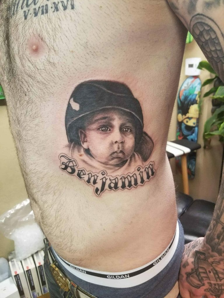 Realistic black and gray portrait tattoo of a young childs face wearing a helmet, with Benjamin written below.