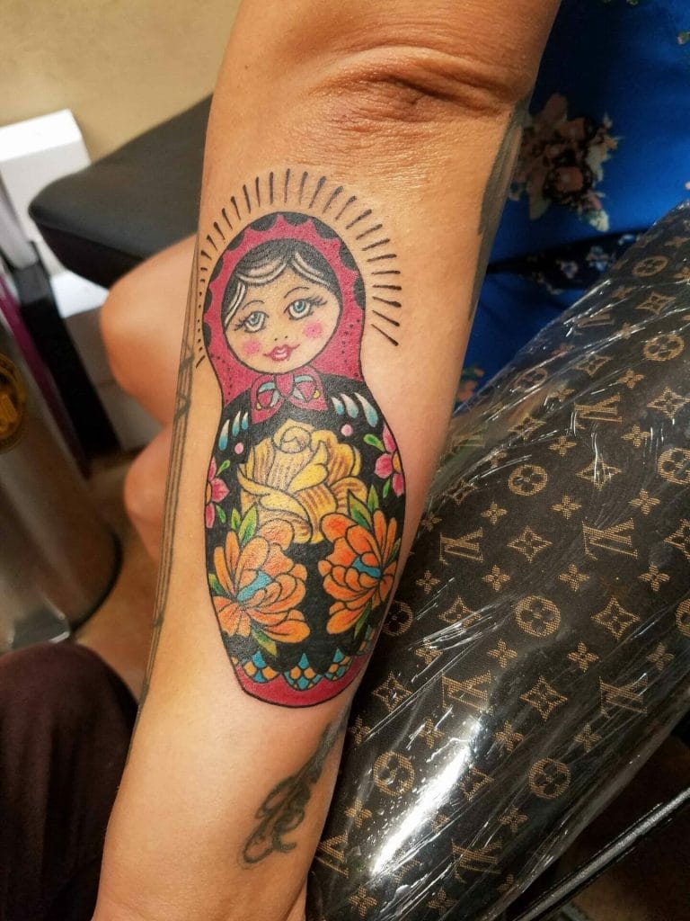 Colorful tattoo of a matryoshka doll with floral patterns on a persons forearm.