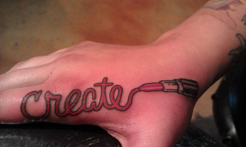 Tattoo of the word create with a paintbrush integrated into the design on a persons wrist.