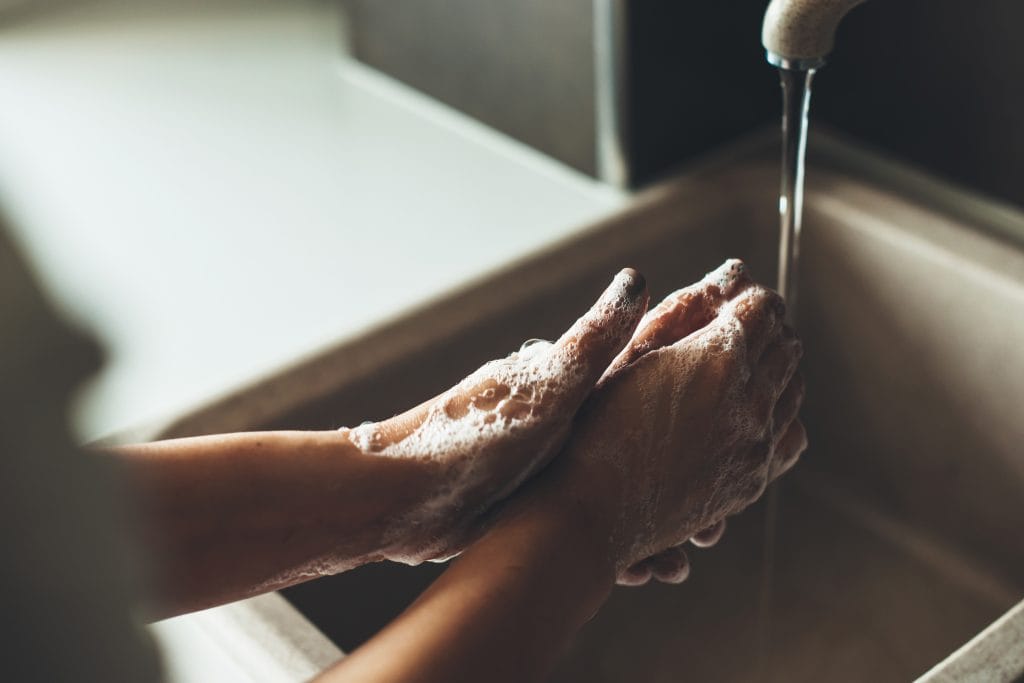 A person lathers their hands with soap under running water at a sink, demonstrating proper handwashing as part of fresh tattoo care.