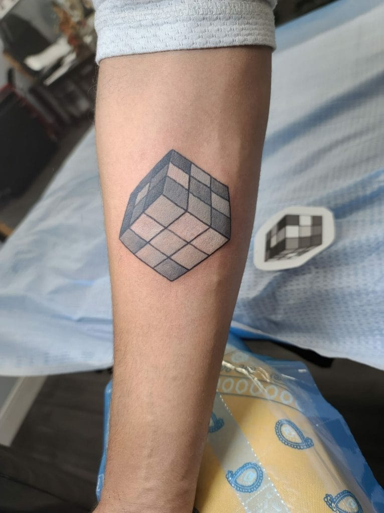 Colorful geometric cube tattoo on forearm with a pixelated sticker nearby.