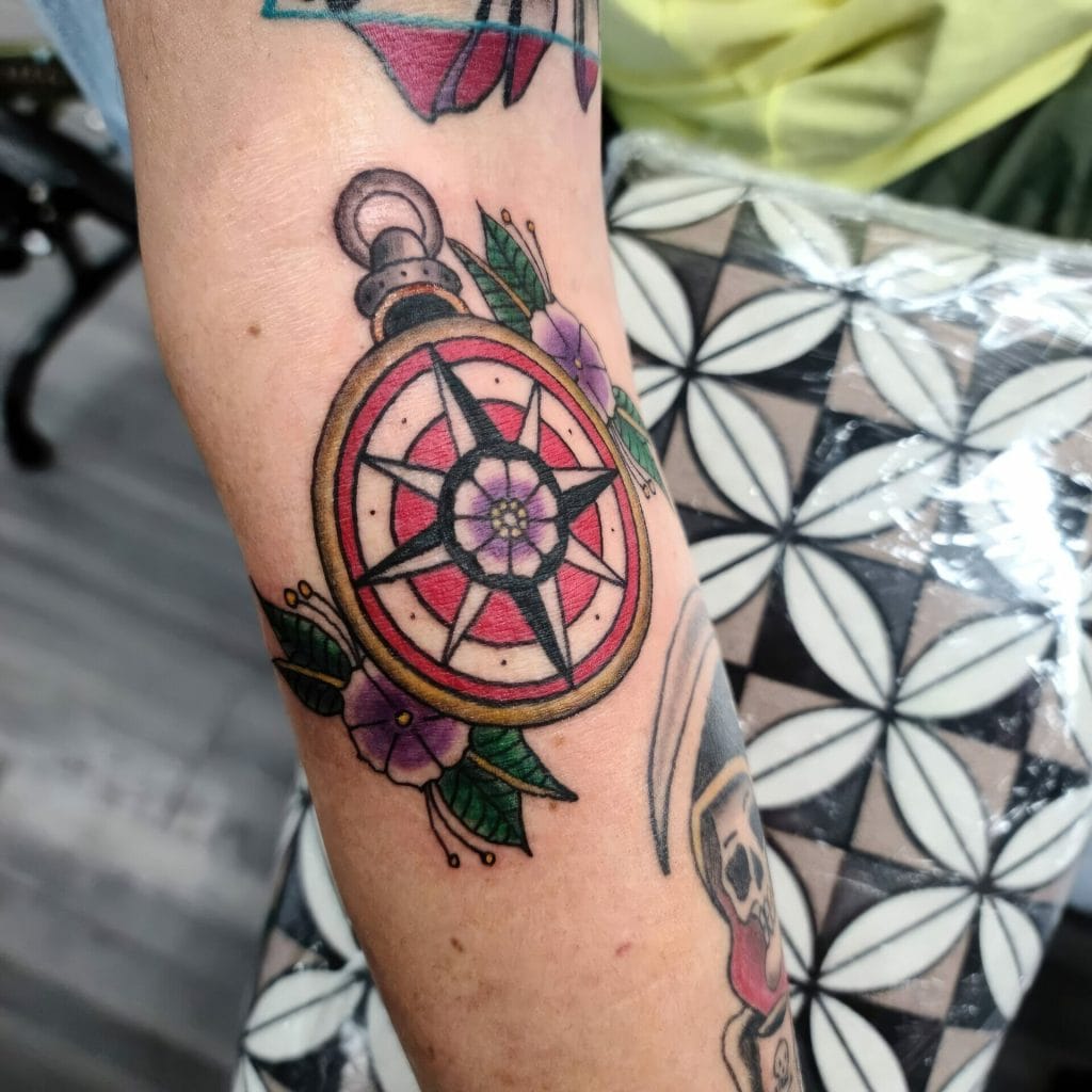 Colorful compass tattoo with purple flowers and green leaves on persons arm.