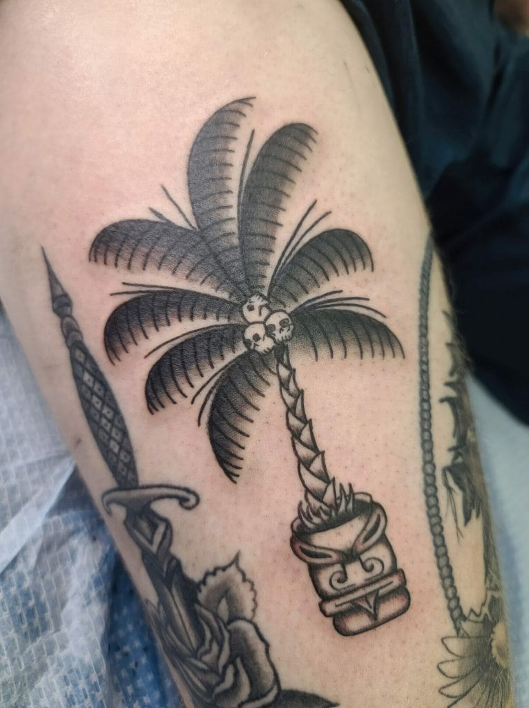 A tattoo of a palm tree with skulls at the base, in black ink on skin.