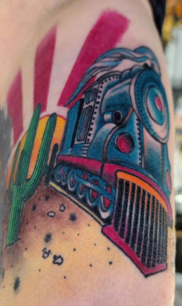 Colorful tattoo of a train engine with desert and cactus background on arm.