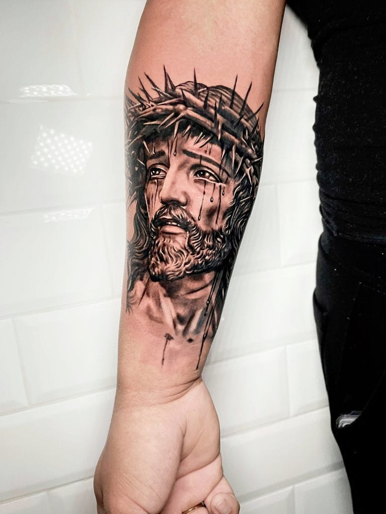 Tattoo of Jesus Christ with a crown of thorns, tears, and detailed shading on the arm.