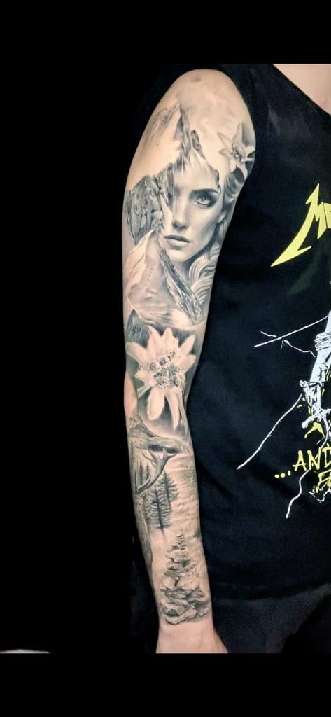 Black and gray realistic tattoo of a womans face, mountains, a flower, and trees on arm.