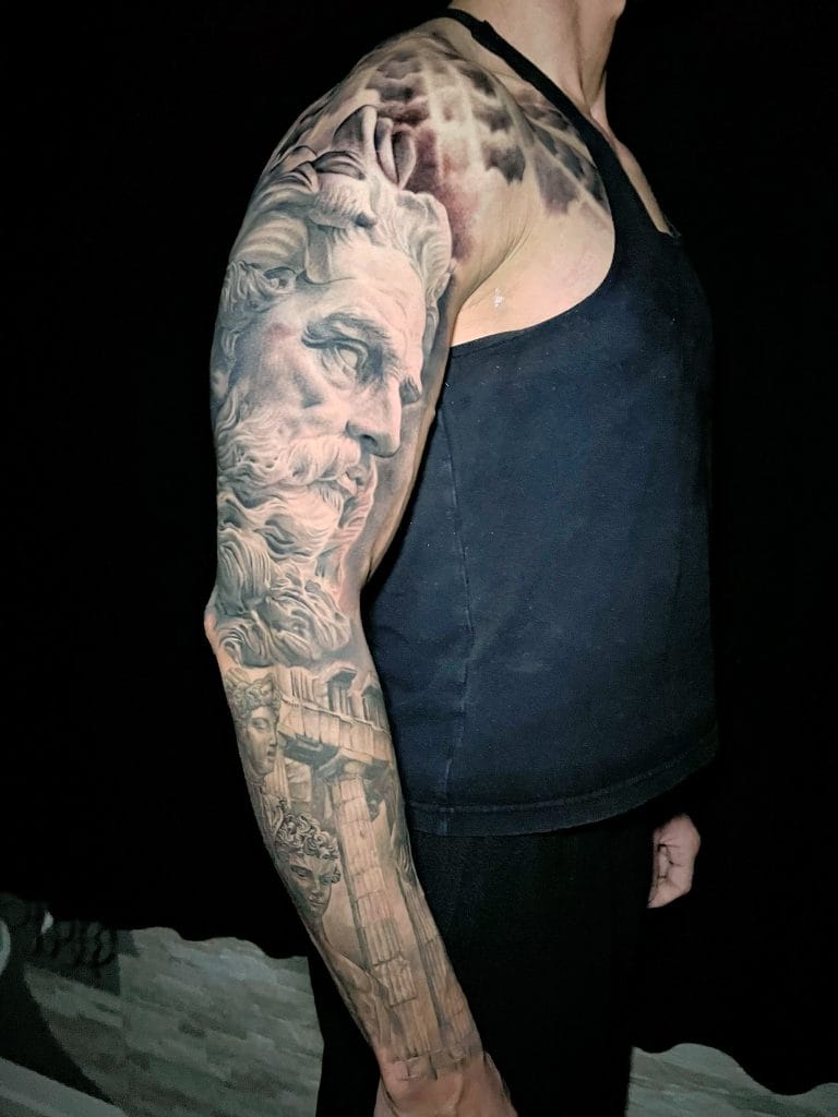 Detailed black and gray tattoo sleeve featuring a classical statue, ancient ruins, and faces.