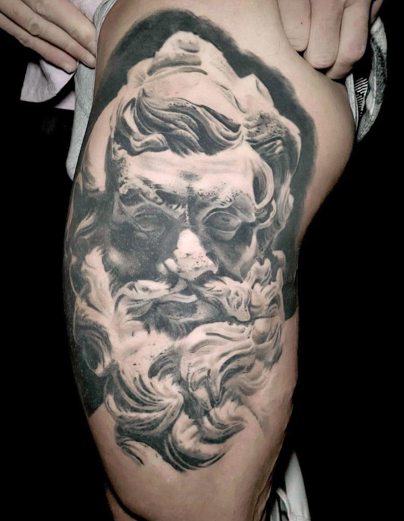 Detailed black and gray tattoo of a classical sculptures face with flowing beard on persons thigh.