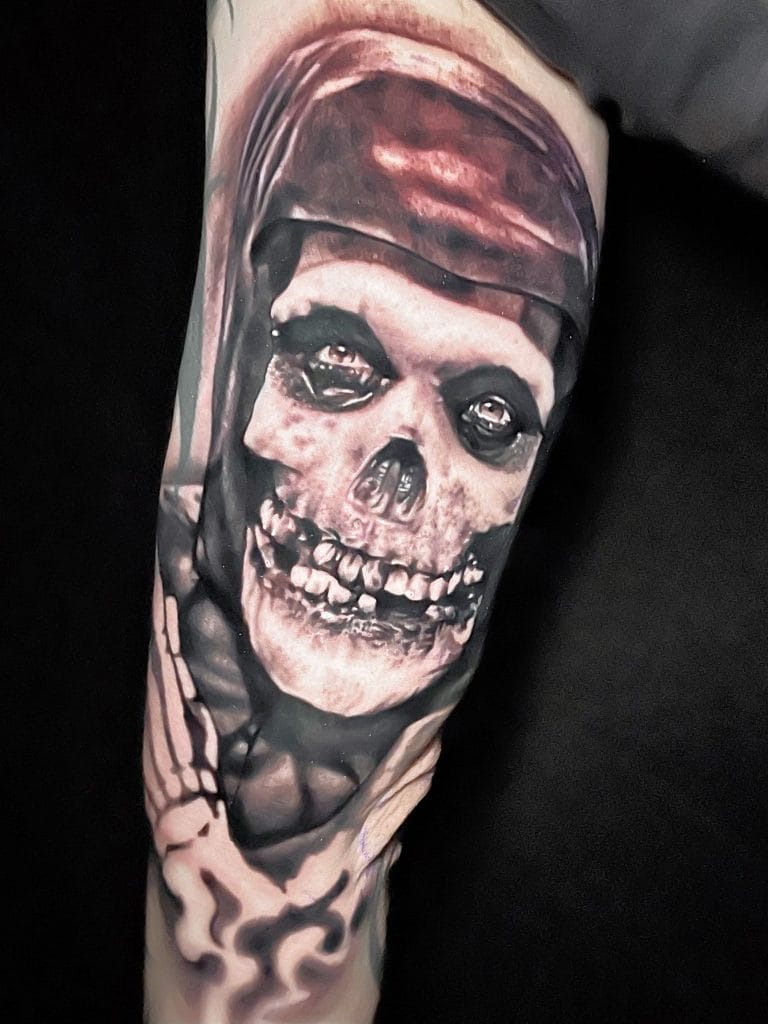 Black and gray tattoo of a skull wearing a bandana, with a skeletal hand below.