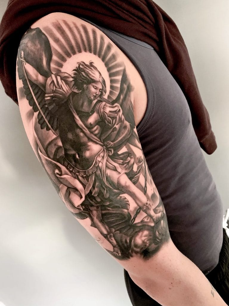 Detailed black and gray tattoo of an angelic figure with wings, halo, and flowing robes.