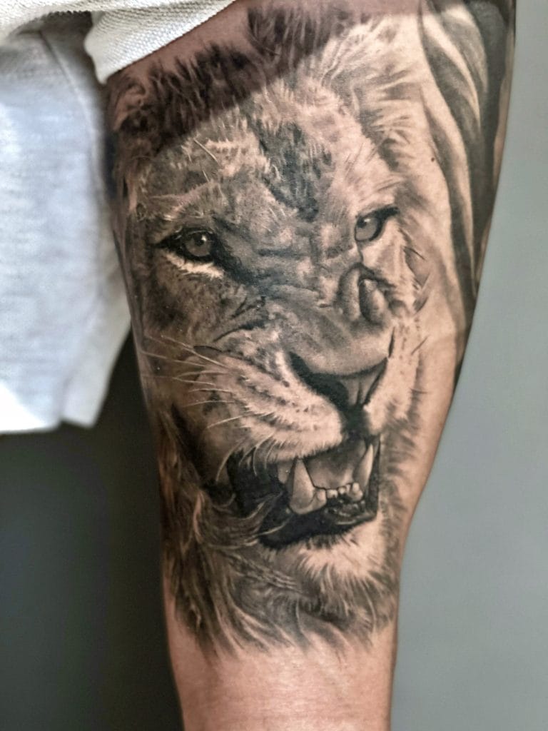 Detailed black and gray lions face tattoo on persons thigh, showing fierce expression.