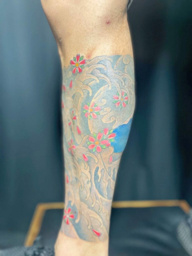 Colorful tattoo of pink flowers and swirling waves covering the lower leg.