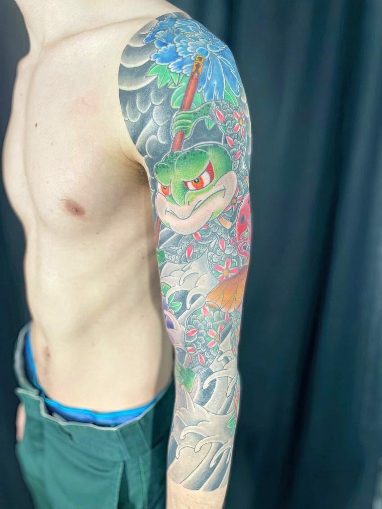 Colorful tattoo of a fierce turtle holding a staff, surrounded by waves and flowers on arm.