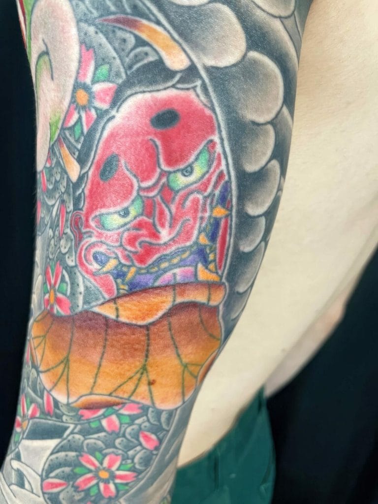 Colorful traditional Japanese Hannya mask tattoo with flowers and a leaf design.