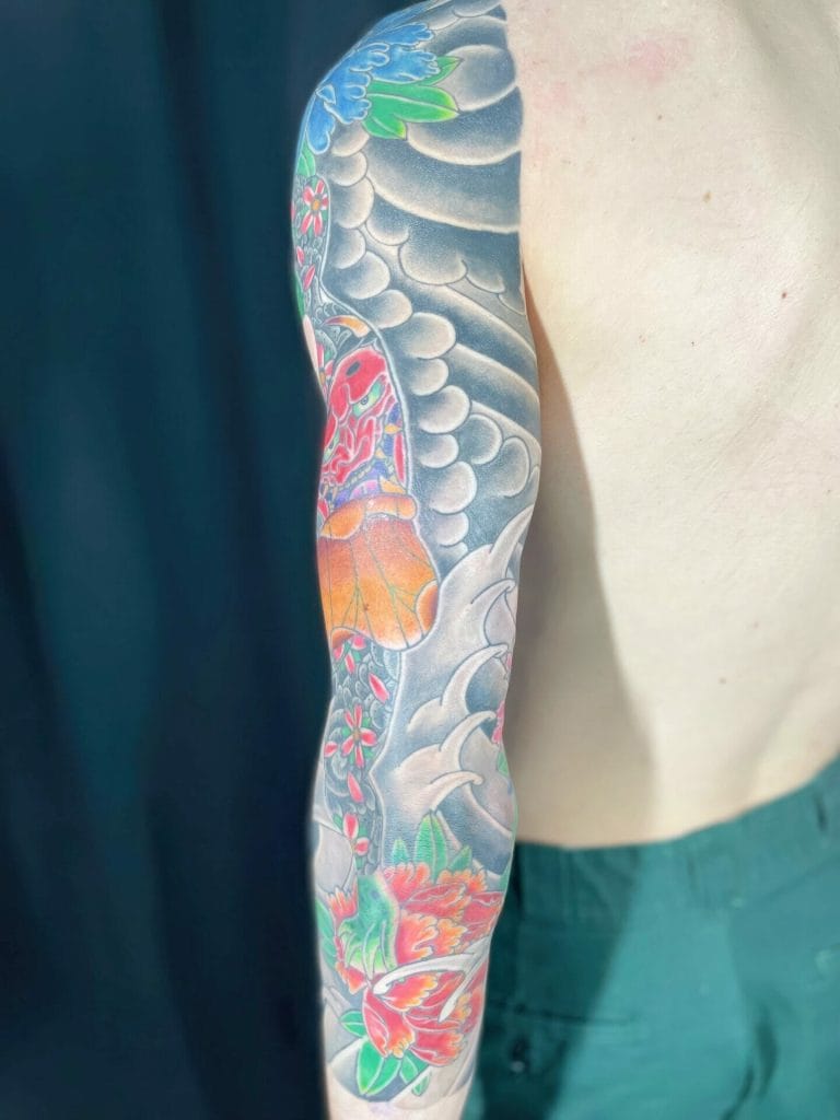 Colorful tattoo sleeve featuring a butterfly, flowers, and abstract designs on persons arm.