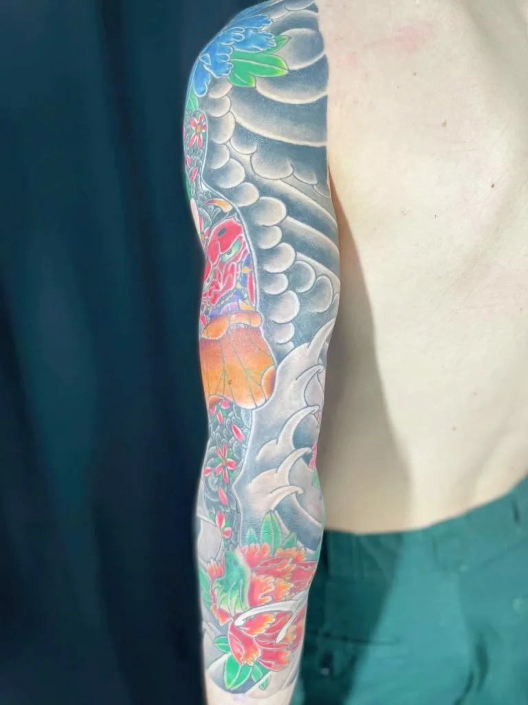 Colorful tattoo sleeve featuring a butterfly, flowers, and abstract designs on persons arm.